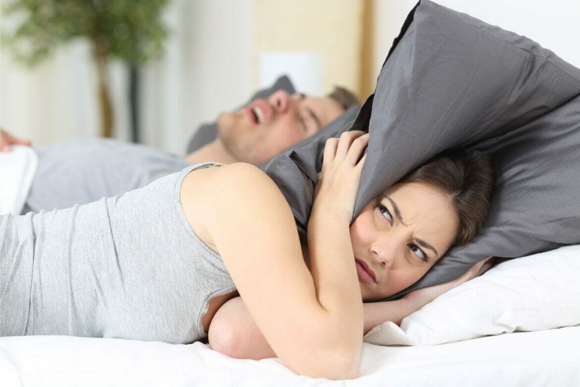 Woman next to snoring man covers her ears with pillow