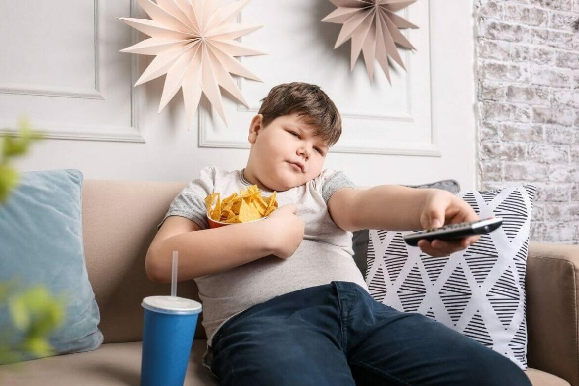 A boy with childhood obesity watching TV and consuming junk food