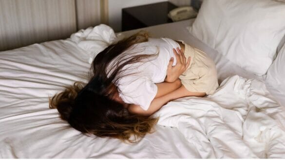 Young woman cuddled on bed with menstrual cramps and period pain