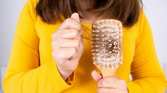Image of a woman holding hairbrush with fallen hair. Regular hair care can ensure good hair health.